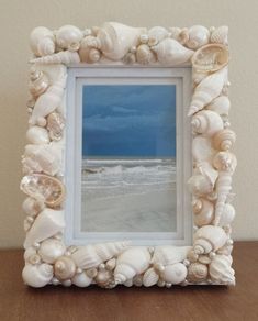 a frame with seashells on it sitting on a table next to the ocean