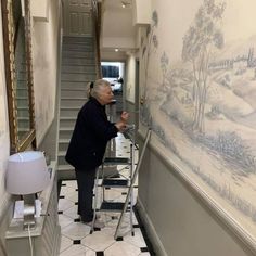 an older man is painting the wall in his house with blue and white mural behind him