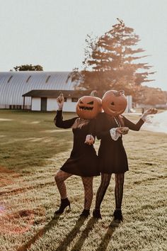 two women in black dresses holding pumpkins on their heads while standing next to each other