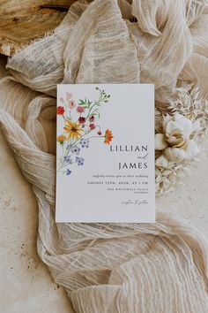 the wedding stationery is laid out on top of sheer fabric and flowers are scattered around it