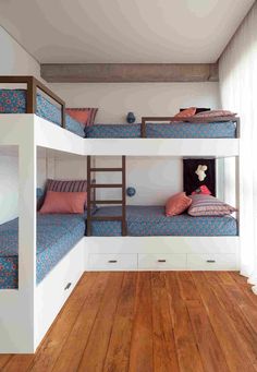 two bunk beds in a room with wooden floors and white walls, one is blue and the other has pink pillows