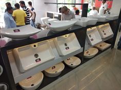 a group of people standing around a bathroom sink with sinks on the wall and bowls on the counter