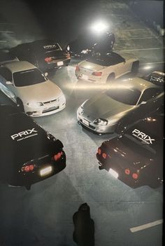 a group of cars parked in a parking lot at night with headlights shining on them