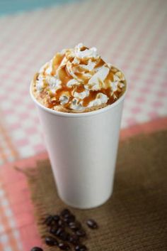 a white cup filled with whipped cream and caramel on top of a checkered table cloth