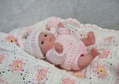 a baby doll laying on top of a crocheted blanket in pink and white