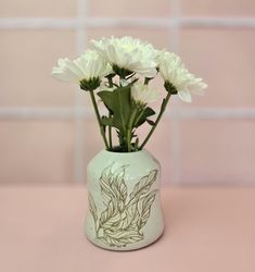 white flowers in a green vase on a pink tableclothed surface with light colored tiles