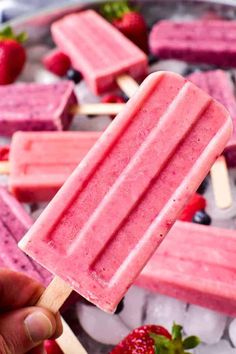 a hand holding a popsicle with strawberries and icecream on the side