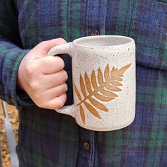 a person holding a coffee mug with a leaf painted on it