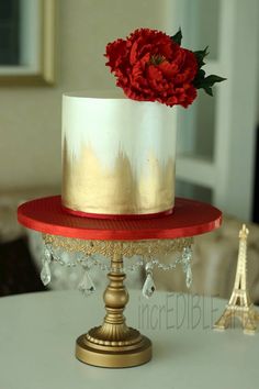 a white and gold cake with a red flower on top