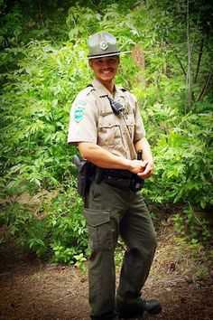 a police officer standing in the woods with his hand on his hip and smiling at the camera