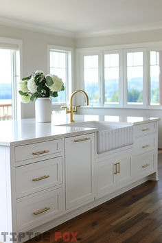 a kitchen with white cabinets and gold handles on the countertop, along with a large vase filled with flowers