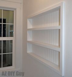 an empty white book shelf next to a window in a room with no one inside