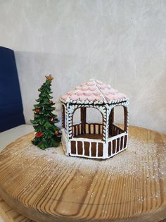 a small gingerbread house next to a christmas tree on top of a wooden table