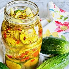 pickles and cucumbers sit in a jar on a floral table cloth next to a flowered napkin