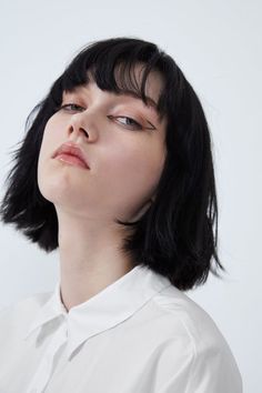 a woman with short black hair wearing a white shirt and looking up at the sky