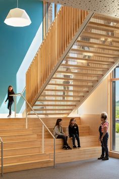 three people sitting on the stairs in a building with glass walls and wooden railings