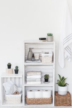 a white shelf with towels, plants and other bathroom items on it next to a wicker basket