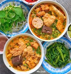 several bowls of food are arranged on the table with green vegetables and sauces around them