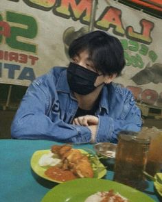 a man wearing a face mask sitting at a table with plates of food in front of him