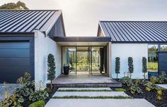 a modern house with two large doors and steps leading to the front door, surrounded by greenery