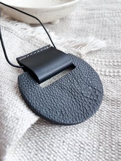 a black piece of leather sitting on top of a white cloth covered table next to a bowl