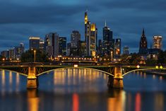 the city skyline is lit up at night with lights reflecting on the water and bridge