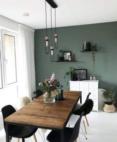 a dining room with green walls and wooden table surrounded by black chairs, vases filled with flowers