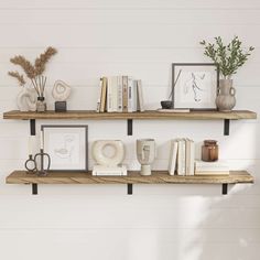 two wooden shelves with books, vases and other items on them against a white wall