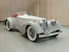 an old model car is parked in a room with some curtains on the wall behind it