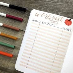 an open planner with markers and pens next to it on top of a wooden table