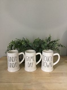 three coffee mugs sitting on top of a wooden table next to a potted plant