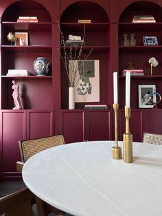 a white table with two candles on it in front of red bookshelves and shelves