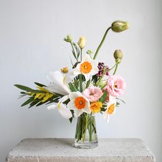 a vase filled with lots of flowers on top of a cement block next to a wall