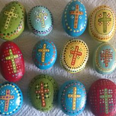 nine painted rocks with crosses on them sitting on a white tablecloth in rows of different shapes and sizes