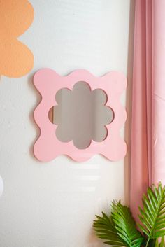 a pink flower shaped mirror mounted to the side of a white wall next to a potted plant