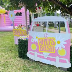 a pink and white van parked under a tree next to some flowers in the grass