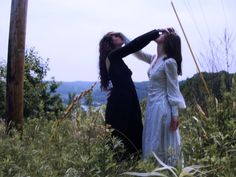 two women are standing in tall grass with their backs to each other and looking into the distance