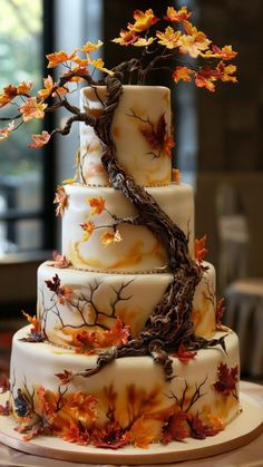 a three tiered wedding cake decorated with fall leaves and an artistic tree branch on top