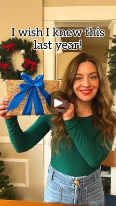 a woman holding up a present in front of a christmas tree with the caption i wish i knew this last year