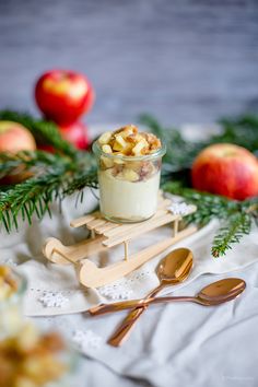 an apple dessert in a small glass on a table with spoons and apples around it