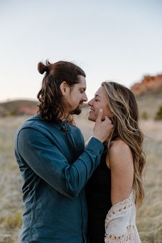 a man and woman standing next to each other in an open field with mountains in the background