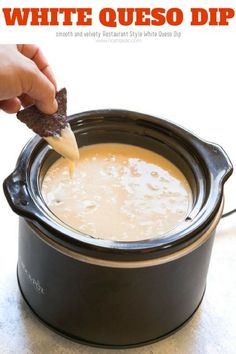 a hand dipping a cracker into a slow cooker filled with white queso dip