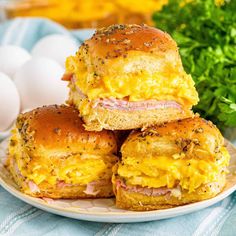 three ham and cheese sliders on a plate next to an egg, parsley