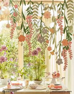 a table with plates and cups on it in front of a window filled with flowers