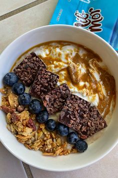 a bowl filled with cereal and blueberries next to a bag of chocolate chip granola