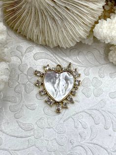 Do you want to make your jewelry stand out from the rest? Look no further than these beautiful Heart Shaped Mother of Pearl Charms! They come in 2 styles and feature a variety of shapes of cubic zirconia making this unique charm a stunner. Choose either Clear CZ or Colorful CZ. Made of gold plated brass, cubic zirconia, and mother of pearl, these charms will add a touch of elegance to any jewelry piece. Plus, orders placed by 11:00 am EST Monday-Friday will ship the same day or the next business Dazzling White Heart-shaped Jewelry, Luxury Pearl Charm Jewelry Made Of Mother Of Pearl, Heart-shaped Pearl Charm Jewelry For Mother's Day, Luxury Heart-shaped Elegant Charms, Heart-shaped Pearl Charm Jewelry, White Heart-shaped Crystal Jewelry, Luxury Heart-shaped Pearl Charm Necklace, Hand Knotted Pearls, Brass Charms