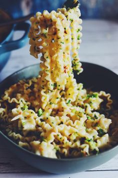 a bowl filled with noodles and broccoli being held up