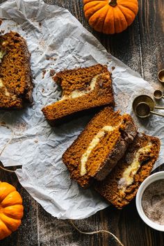 slices of pumpkin bread with white frosting on a piece of parchment paper next to some small pumpkins