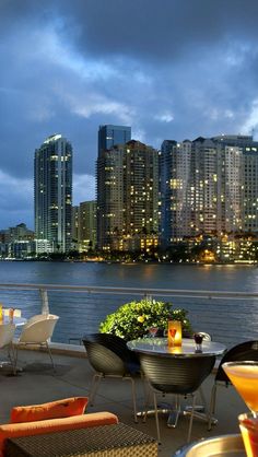 an outdoor dining area overlooking the water with city lights in the background