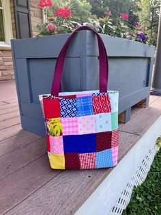 a multicolored patchwork bag sitting on the ground next to a planter